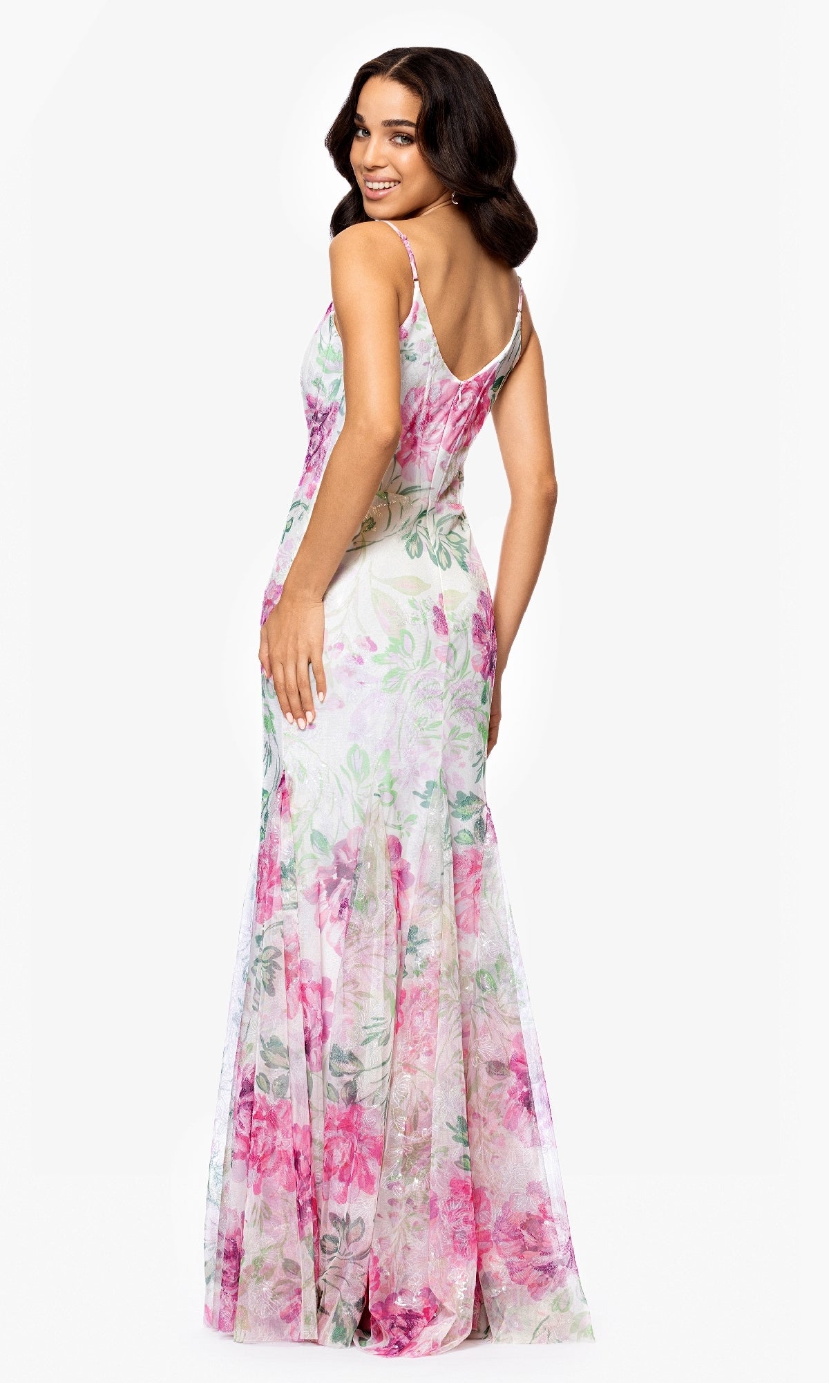 Woman standing and smiling, photographed from the back in a Betsy and Adam A27020 Long Ivory Print Prom Dress, a sleeveless floor-length gown with pink and green floral pattern, against a white background.